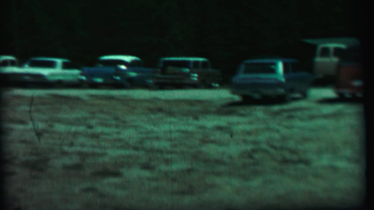 1967 home-movie frame from Farragut State Park showing several parked cars on a gravel lot under dark, green-tinted exposure.
