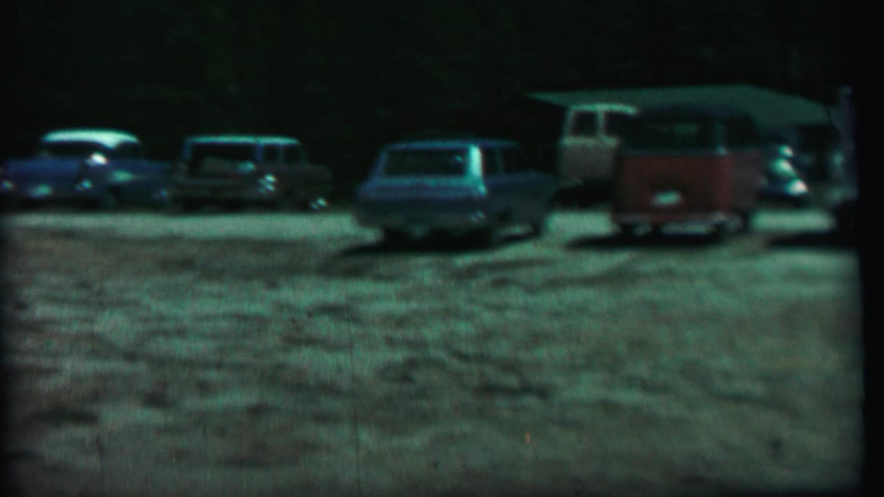 Line of parked cars and a red-and-white van at the edge of a gravel lot.