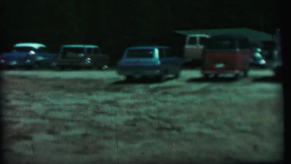 A slow pan reveals parked 1960s vehicles at Farragut State Park, including a red-and-white van near the right side of the gravel lot.