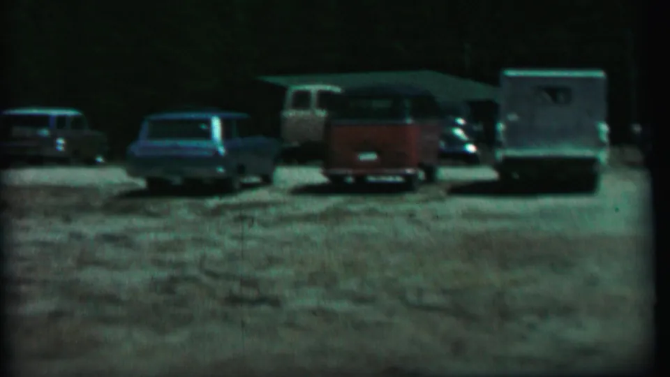 Farragut State Park parking area with vintage cars, a red-and-white van, and a trailer or camper visible in soft 8mm color.
