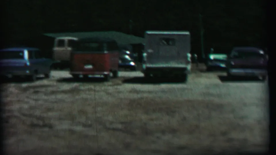Final frame of the pan across a 1967 Farragut State Park gravel lot, with a red-and-white van, trailer or camper, and additional parked cars.