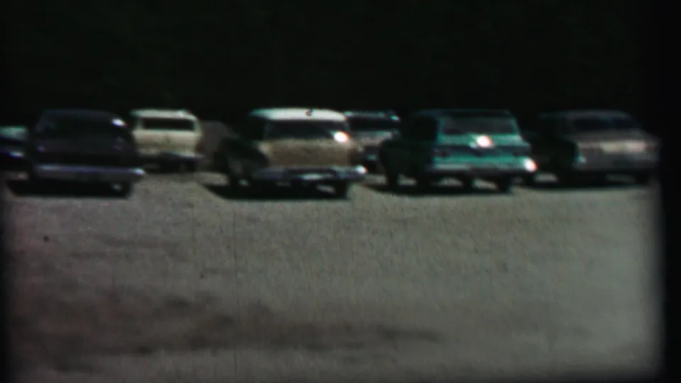 1967 home-movie frame showing a row of 1960s-style parked cars at Farragut State Park, including light and dark wagons near a wooded background.