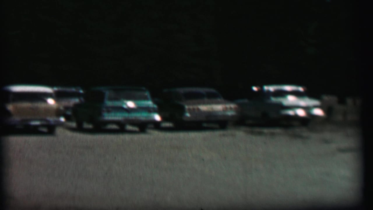 1967 8mm frame from Farragut State Park metadata showing a row of mid-century American cars parked across a dark tree-lined lot.