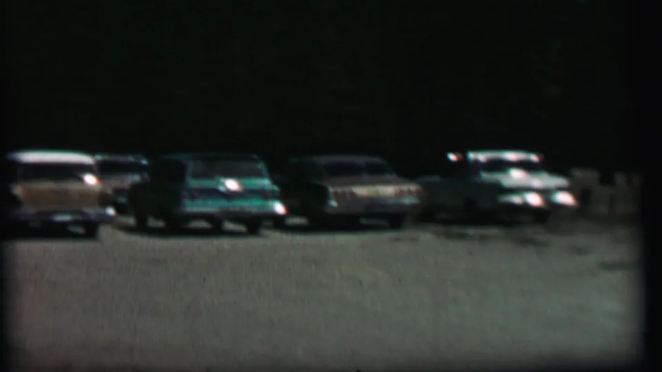 1967 8mm frame from Farragut State Park metadata showing a row of mid-century American cars parked across a dark tree-lined lot.