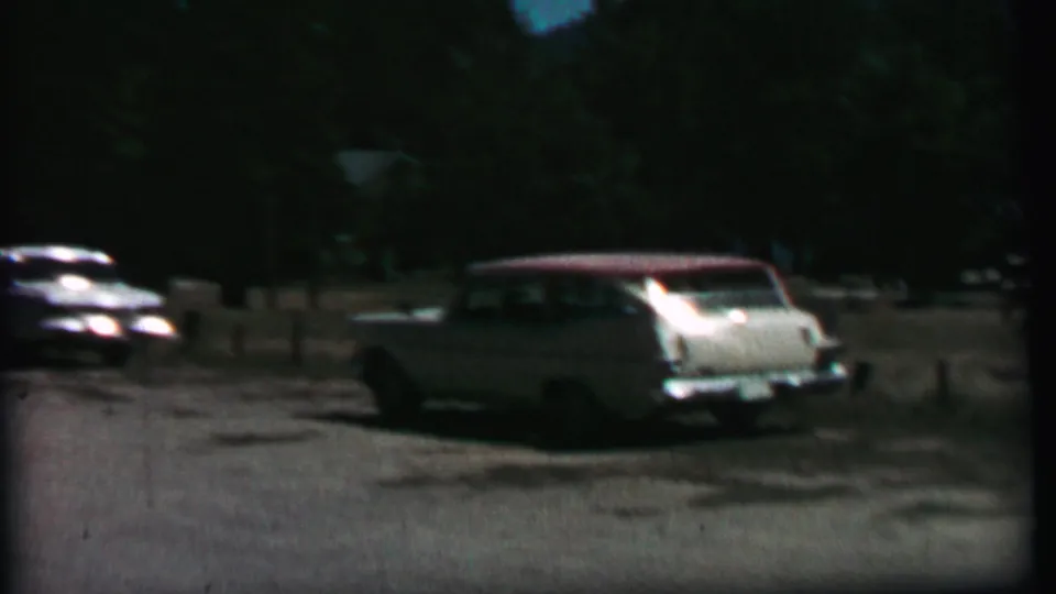 A grainy 8mm frame shows a light station wagon in the foreground at Farragut State Park in 1967, with a darker parked car and wooded background.