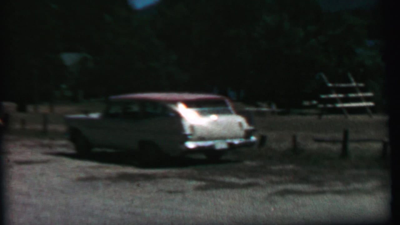 1967 Farragut State Park home-movie frame showing a white station wagon with a red roof near a split-log fence, picnic tables, gravel, and trees.