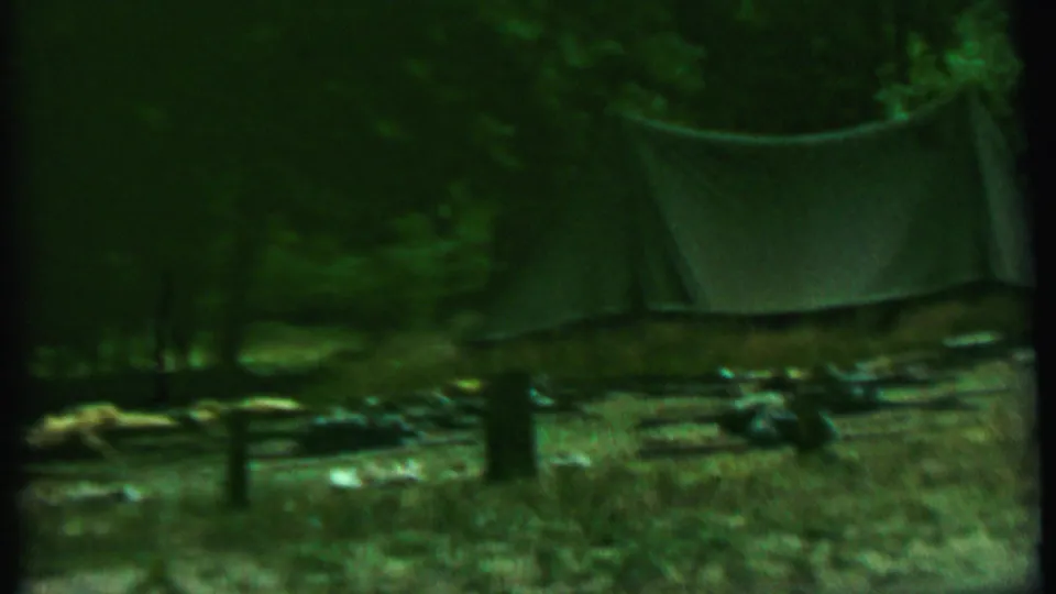 Mid-1960s 8mm frame of the Farragut State Park campsite with the canvas tent, trees, fence posts, and gear visible in soft green-tinted light.