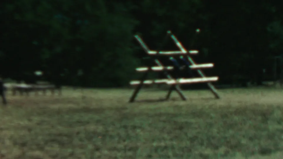 Final 8mm frame holds on the rustic wooden picnic structure in a grassy Farragut State Park clearing, with a soft dark tree line behind it.