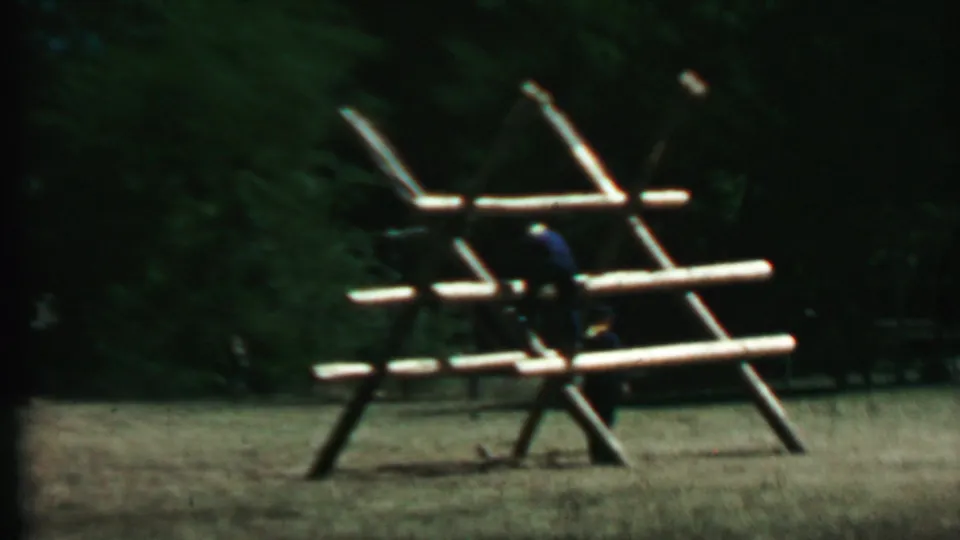 People, likely children or young visitors, climb and stand around the wooden trellis-style play structure in the 1967 Farragut State Park home-movie footage.