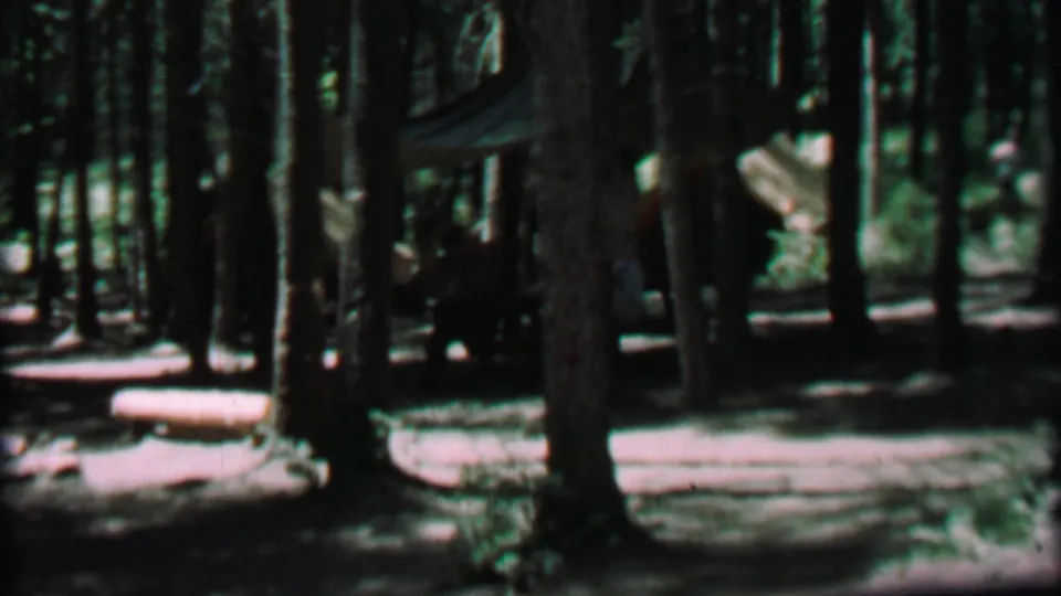 1967 Farragut State Park campsite frame showing a tent tucked between pine trunks, a picnic table, logs, and a shaded dirt clearing.
