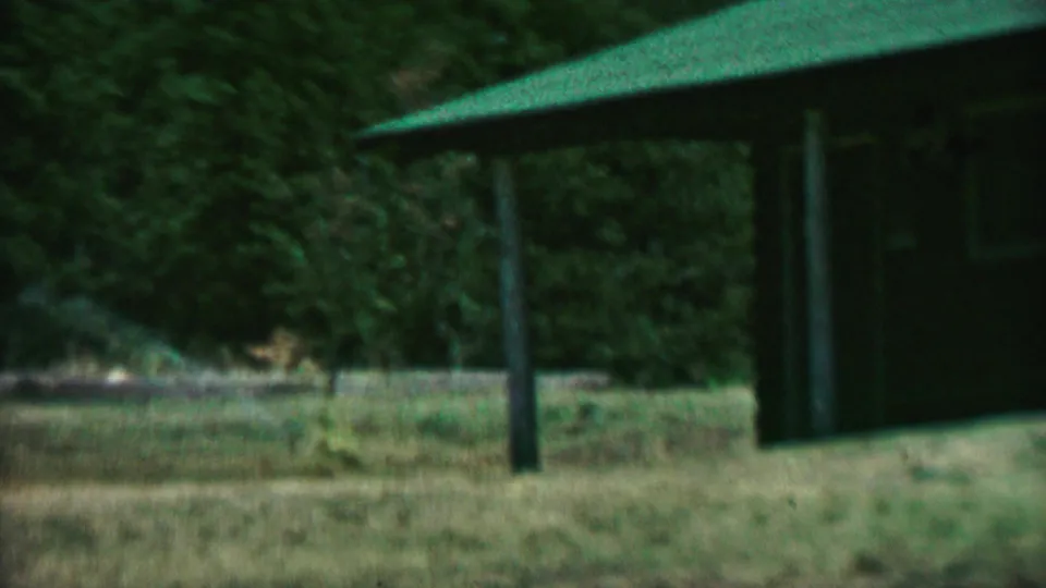 Farragut State Park building with a green roof, dark siding, grassy ground, and dense trees, recorded in soft 1960s 8mm color.