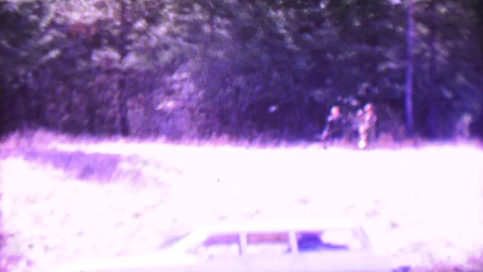 Overexposed 1967 home-movie frame showing a white station wagon in a grassy area with distant people near the tree line at Farragut State Park.