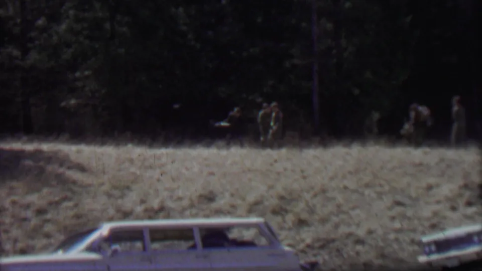 Supported by the supplied location and year, this frame shows a vintage station wagon parked below a grassy field as several people move near the tree line at Farragut State Park in 1967.