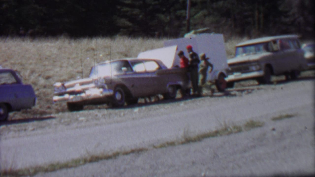 1967 Farragut State Park frame showing two travelers beside a mid-century sedan with its trunk open, with a small trailer and station wagon parked nearby.