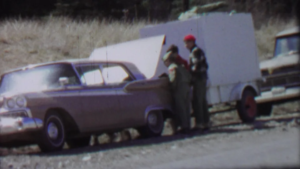 Close 1967 Farragut State Park frame showing two people at the rear of a vintage sedan with the trunk open, filmed on soft color 8mm beside a rural road.