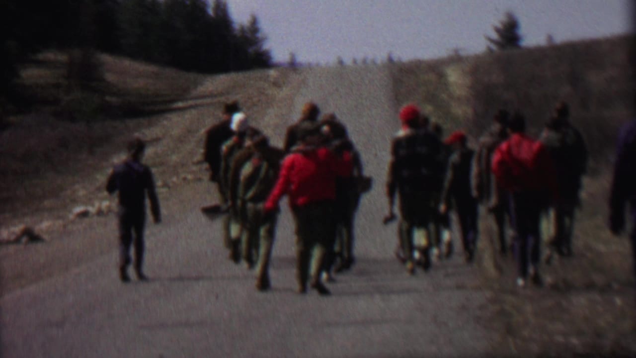 Walkers in outdoor gear continue along the road with a light-colored station wagon ahead.