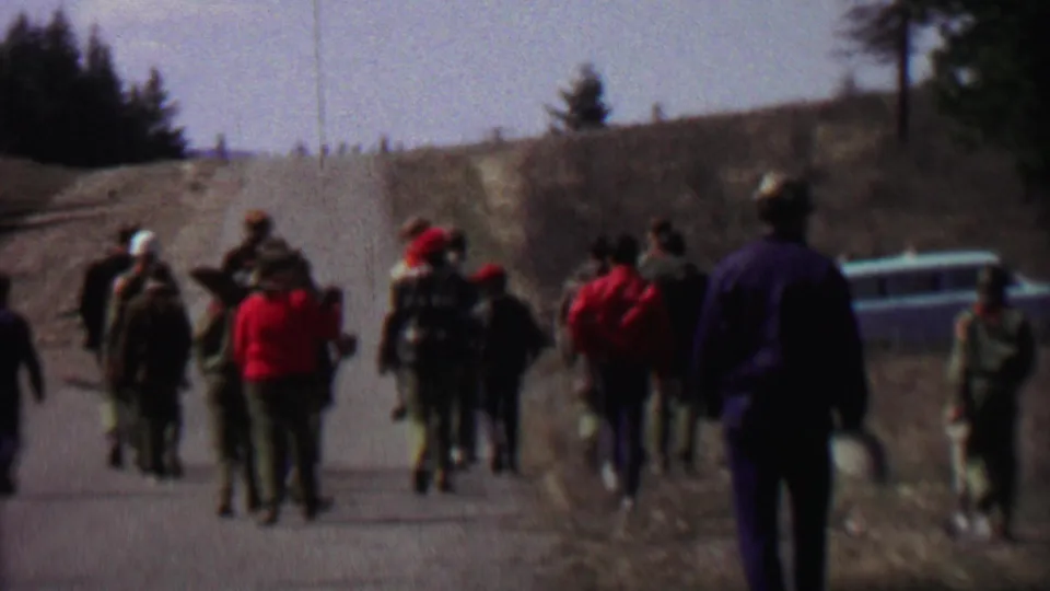 A closer rear view shows the group moving along the rural Farragut State Park road, with red caps, backpacks, and carried shovels or axes visible in the 8mm frame.