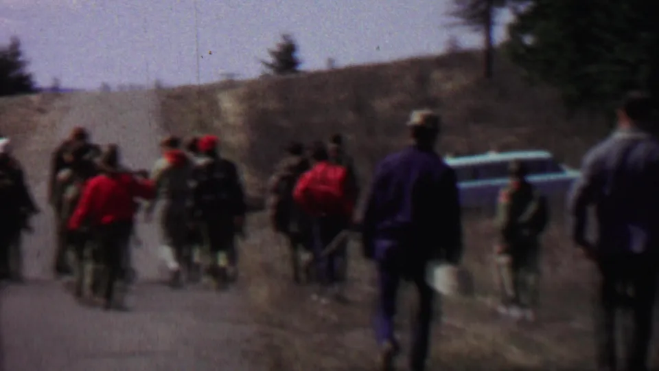 Near the end of the clip, the group appears to gather or slow beside a light-colored station wagon on the rural road, with pines and dry hillside terrain in the background.