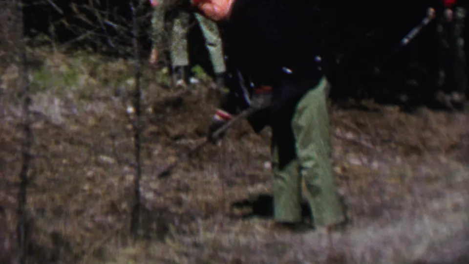 The 1967 Idaho park scene shows the worker partly framed by bare saplings as he holds a long-handled tool over dry ground and brush.