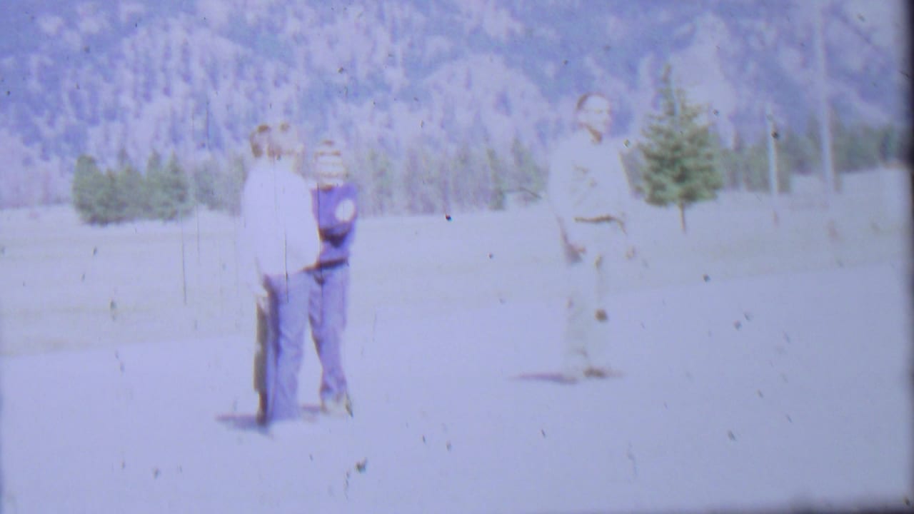 1967 8mm frame from Farragut State Park metadata showing two adult men together at left and another man farther right, with evergreens and mountains behind them.