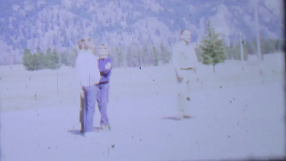 1967 8mm frame from Farragut State Park metadata showing two adult men together at left and another man farther right, with evergreens and mountains behind them.