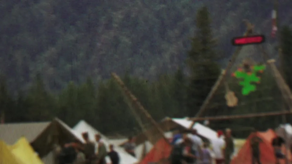 Festival visitors move around tents near a teepee-style Mexico display at Farragut State Park, with forested hills behind the campsite area.
