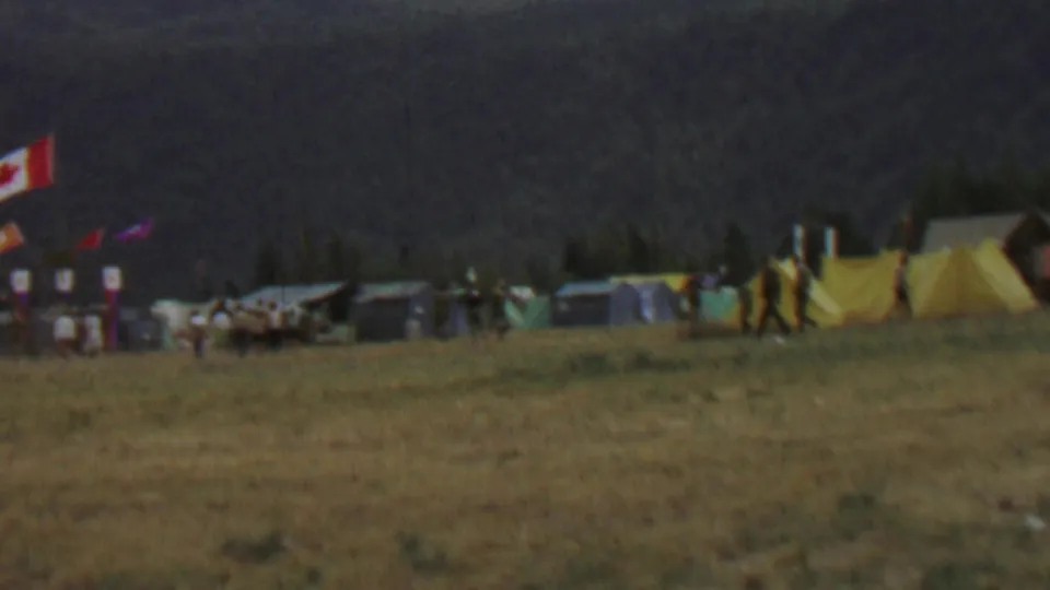 Wide Farragut State Park festival campsite scene showing yellow tents, flags, people walking, and low camp structures against a dark wooded hillside.