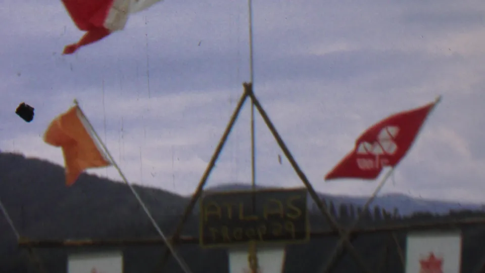 A wider 1967 Idaho camp view shows multiple wooden tripod frames with Atlas Troop 29 signs and red and orange flags moving in the wind.