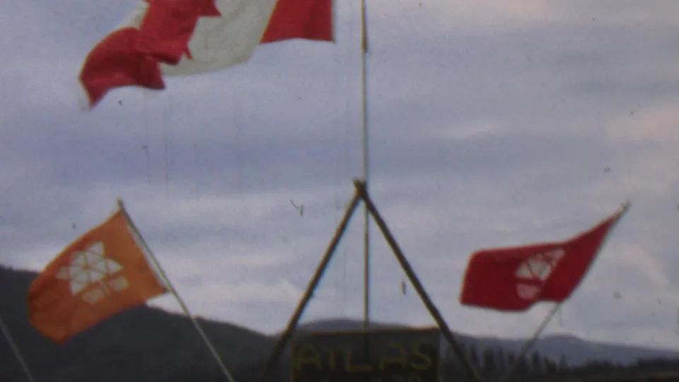 The 8mm frame centers on a hand-painted Atlas Troop 29 sign beneath a wooden tripod, with red and orange flags and the Idaho landscape in the background.
