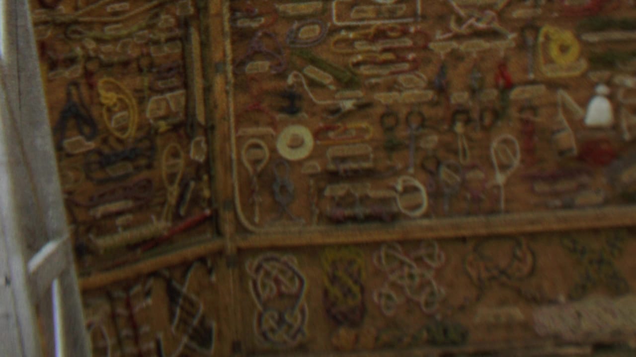 1967 8mm frame from Farragut State Park, Idaho, showing a close, soft-focus view of ornate embroidered or stitched wall decoration beside a pale vertical frame.