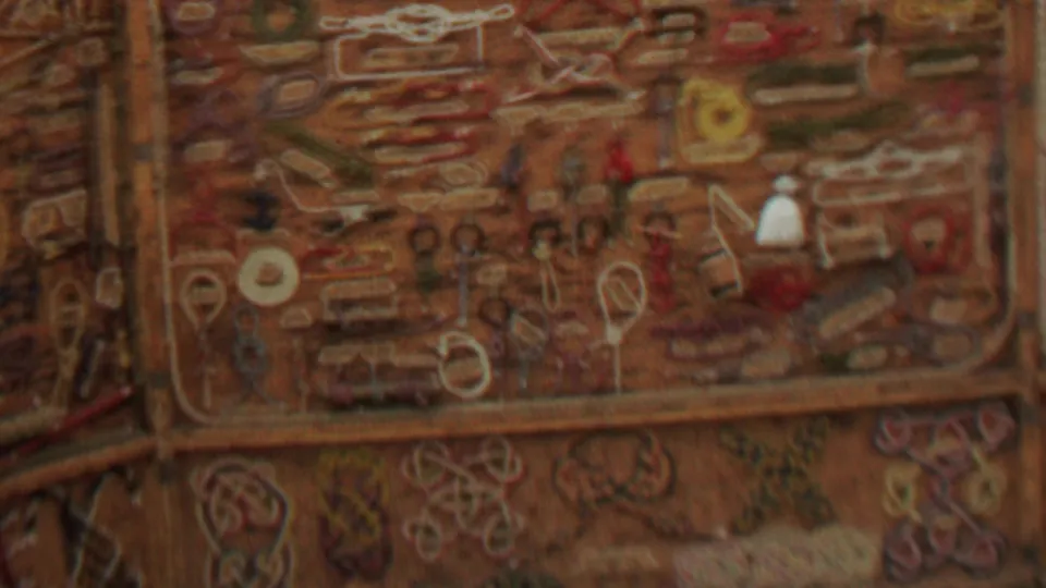 Close 8mm frame of the ornate wall covering, emphasizing colored stitching, looped designs, and a soft, grainy indoor home-movie look from the 1967 Idaho park footage.