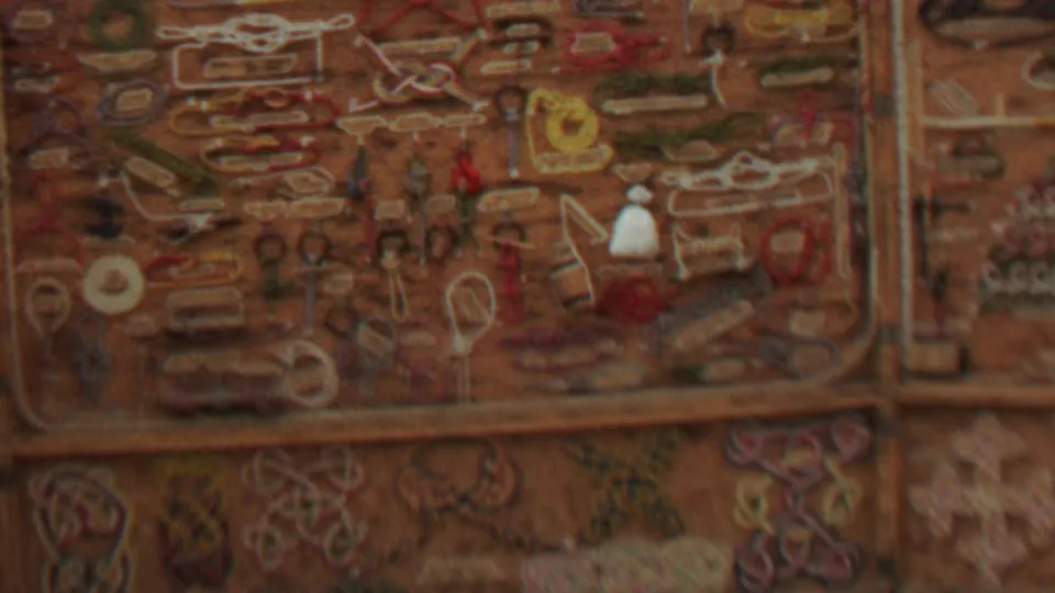 Final 1967 home-movie frame showing the embroidered or stitched wall decoration with repeated motifs, warm faded color, and vertical trim within an interior at Farragut State Park, Idaho.