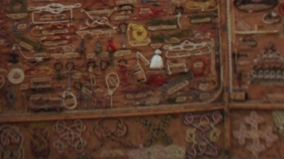1967 United States 8mm frame showing a warm-toned handmade craft display with embroidered shapes, trinkets, and jewelry-like objects arranged in a grid.