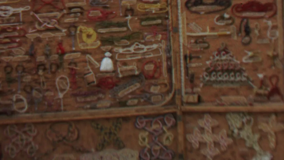 Soft-focus 1967 home-movie frame showing a rustic display of handmade ornaments, stitched forms, and jewelry-like craft items in warm brown tones.