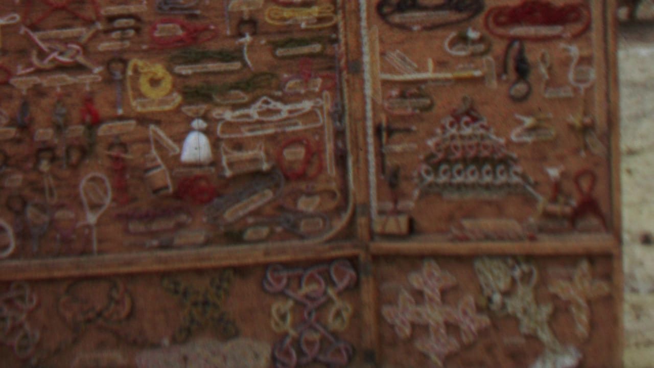 Close 1967 8mm frame of weathered decorative panels with raised shapes and muted red, tan, and cream colors, likely part of the same rustic outdoor structure.