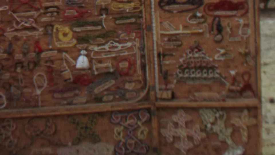 Close 1967 8mm frame of weathered decorative panels with raised shapes and muted red, tan, and cream colors, likely part of the same rustic outdoor structure.