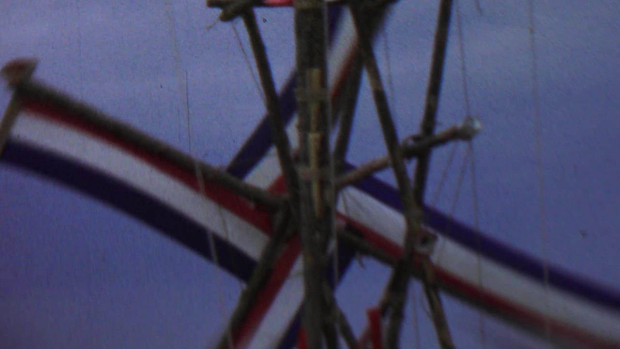 Close-up of a wooden windmill-like frame with red, white, and blue striped fabric against the sky.