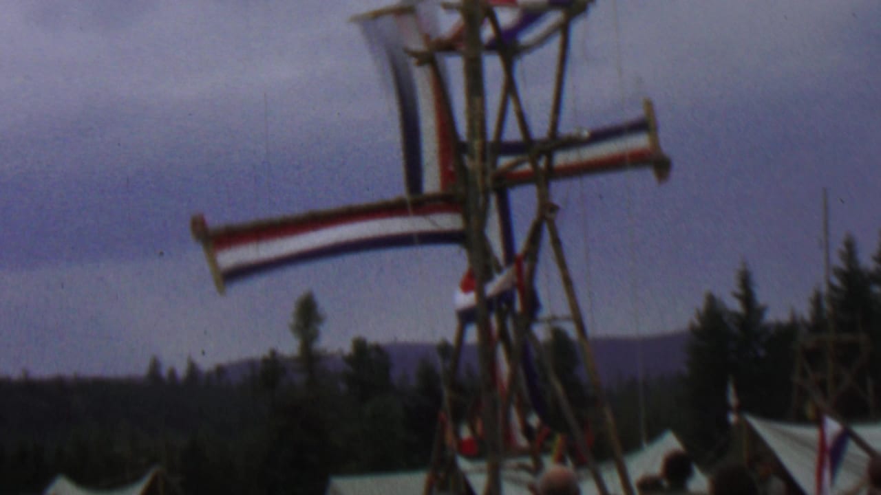 1967 8mm frame from Farragut State Park, Idaho, showing a wooden Dutch-style windmill display with red, white, and blue striped sails over festival tents and evergreens.