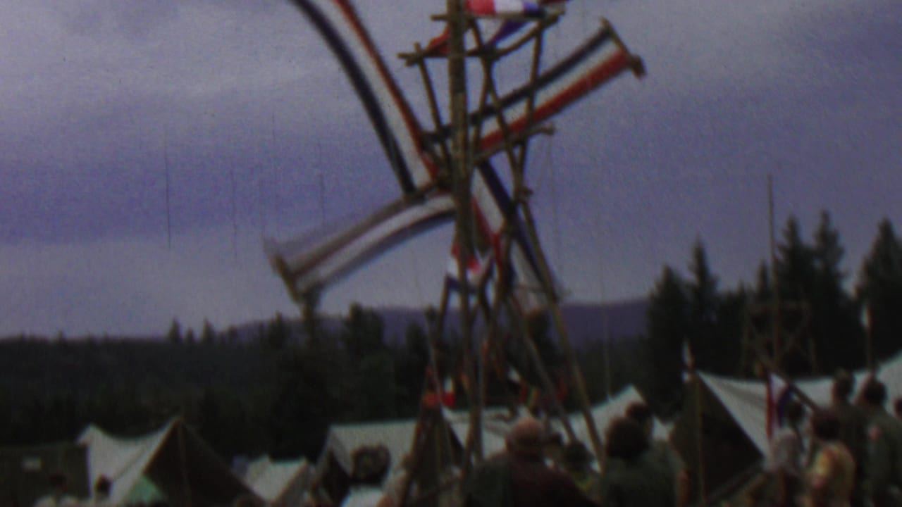 1967 Farragut State Park home-movie frame showing the Dutch-style windmill sails mid-rotation with white tents, trees, and distant hills behind them.