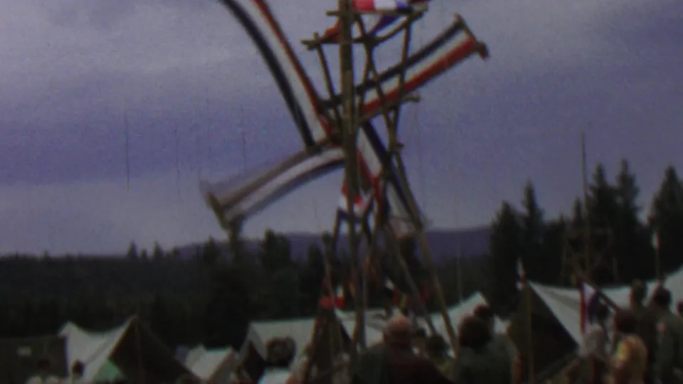 1967 Farragut State Park home-movie frame showing the Dutch-style windmill sails mid-rotation with white tents, trees, and distant hills behind them.