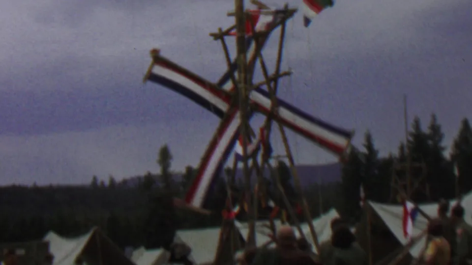 1967 8mm frame showing the wooden festival windmill at Farragut State Park with striped sails, tent tops, and partially visible visitors beneath an overcast sky.