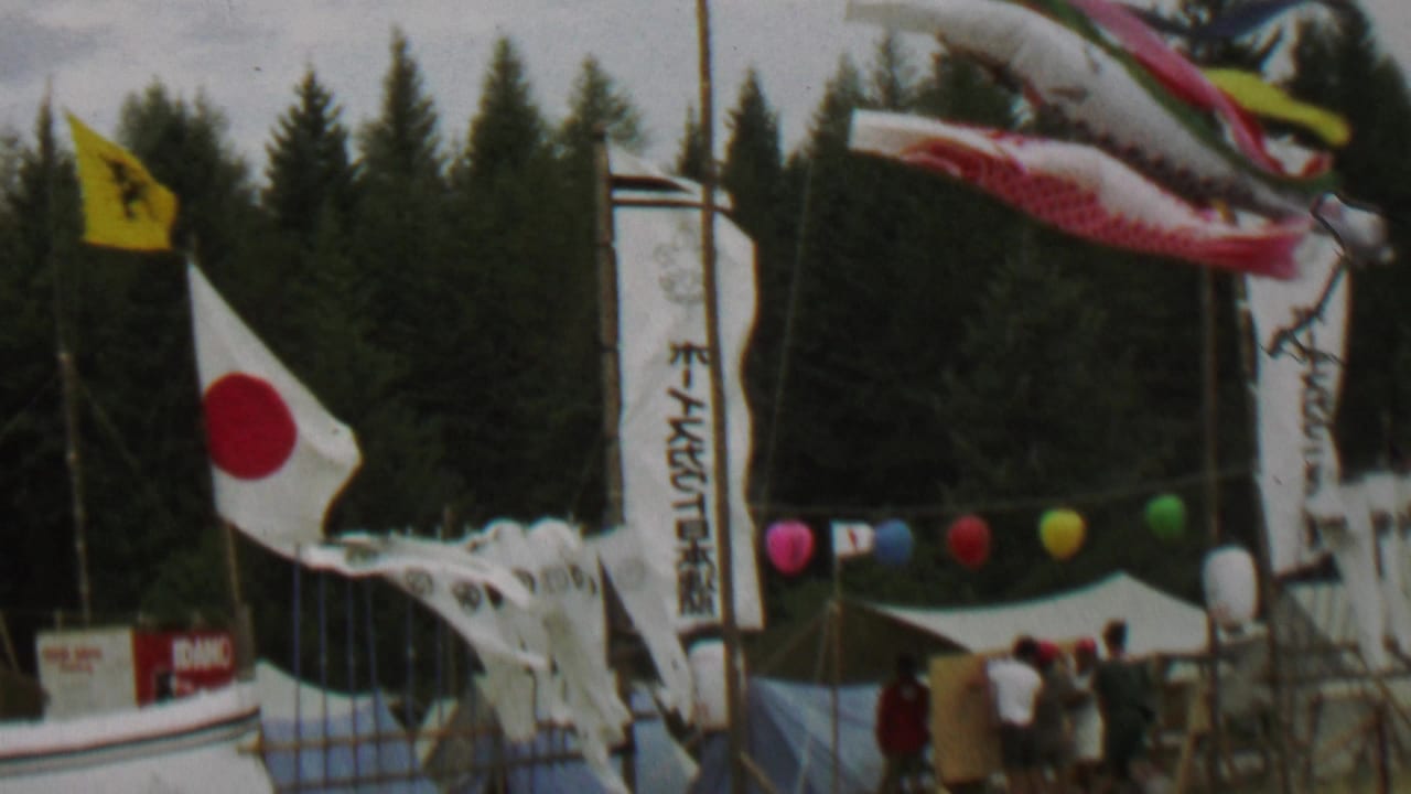 1967 Farragut State Park footage shows a Japanese flag, windblown carp streamers, vertical banners, tents, balloons, and attendees near evergreen trees.