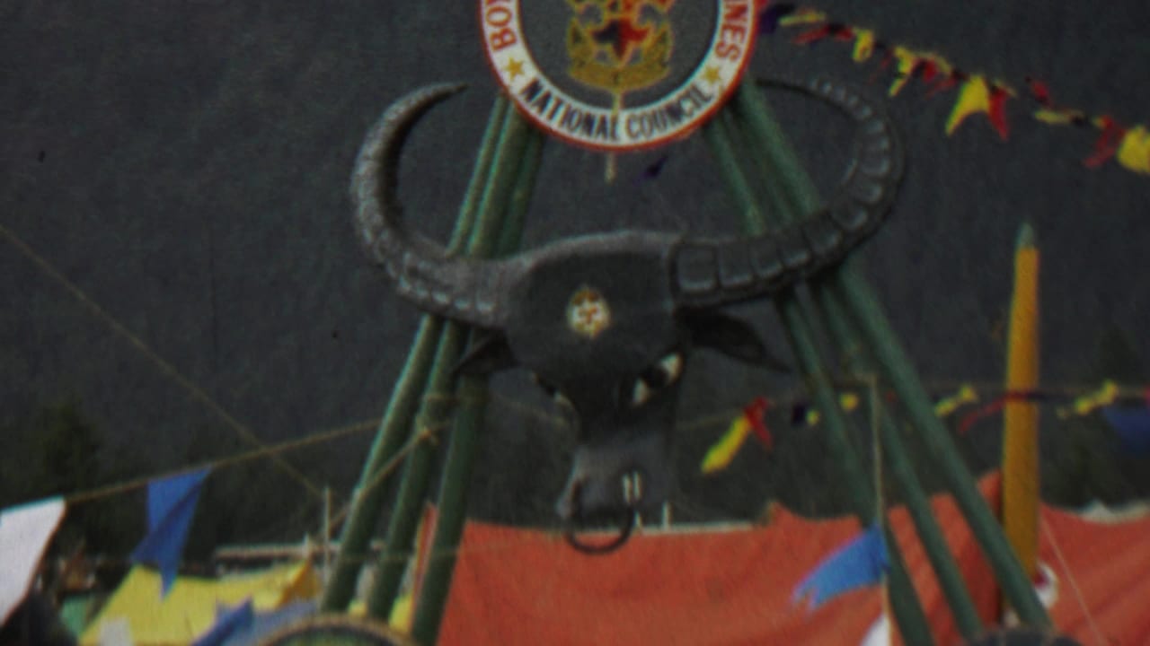 1967 8mm frame from Farragut State Park showing a large black bull's head mounted below a Boy Scouts of the Philippines National Council emblem, with colorful pennants and orange fabric visible around the structure.