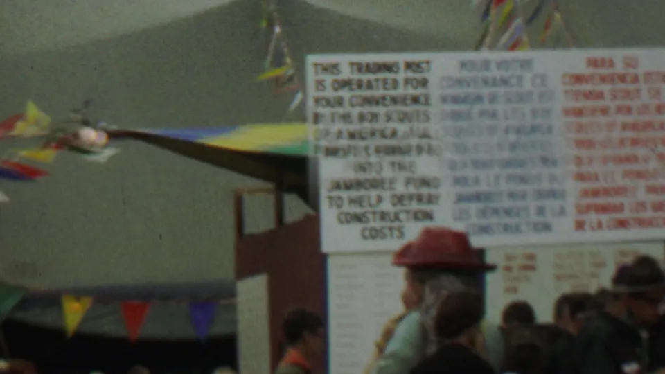 Soft 8mm frame of the 1967 Boy Scouts trading post sign at Farragut State Park, partly obscured by visitors and colorful pennants.