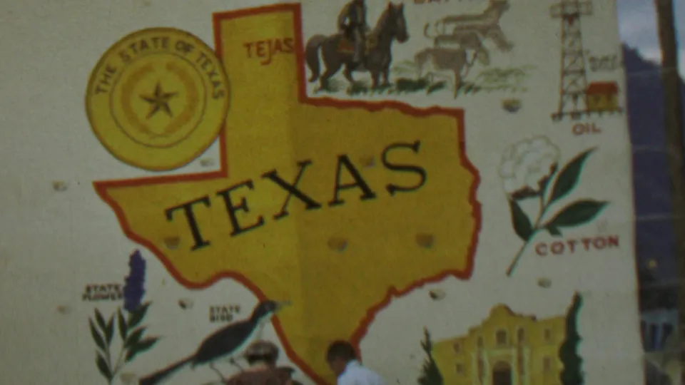 1967 8mm home-movie frame showing a Texas souvenir poster in close view, with two people partly visible along the lower edge beneath the map and Alamo illustration.