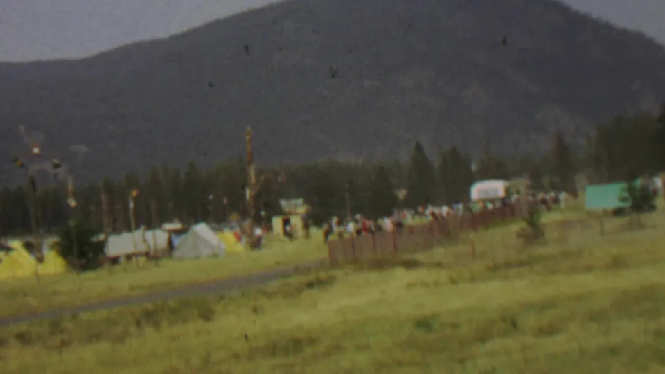 1967 8mm view of a grassy field at Farragut State Park with small tents, distant people, flags, trees, and mountains in the background.
