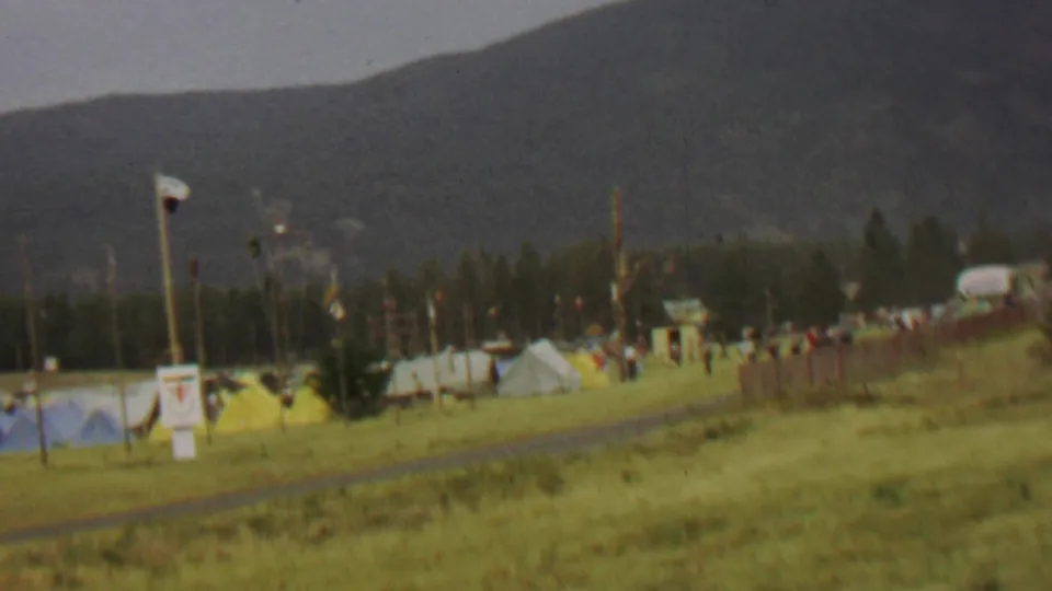 At Farragut State Park in 1967, a flagpole stands near tents and scattered people on a grassy field with wooded hills and mountains beyond.