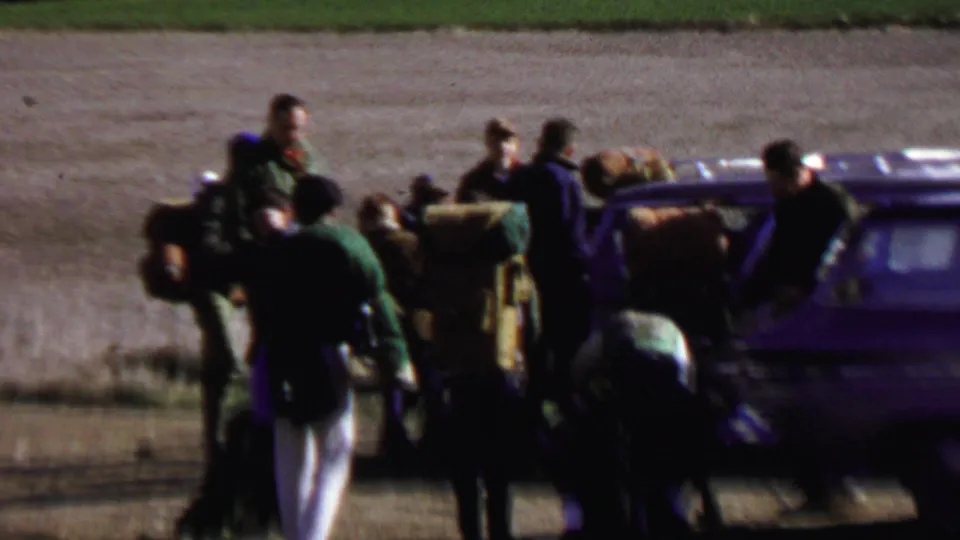 Close end-frame view of the group clustered around a station wagon with visible backpacks and bundled camping gear during a 1967 Idaho park outing.