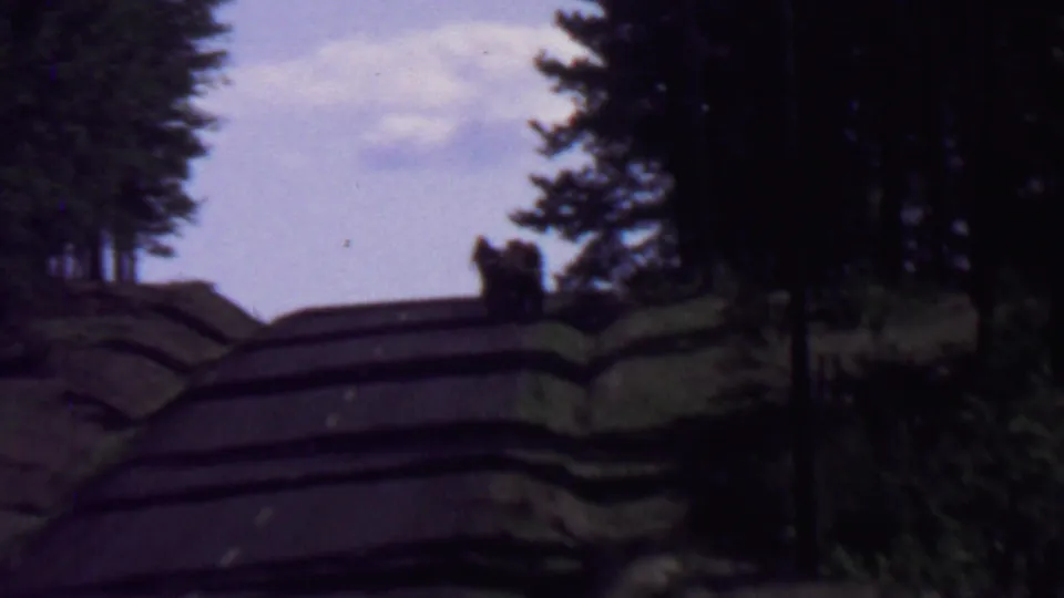 Distant visitors appear near the top of a winding road in supported 1967 Farragut State Park footage, with heavy tree shadows and soft 8mm color.