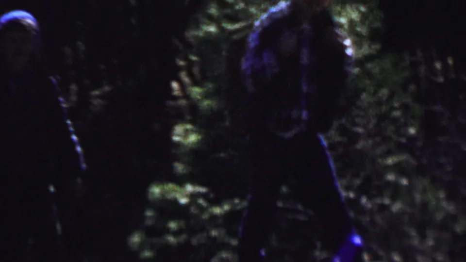 A hiker with a large backpack stands or walks in dense Idaho forest shade in this final 1967 home-movie frame from the supplied clip.